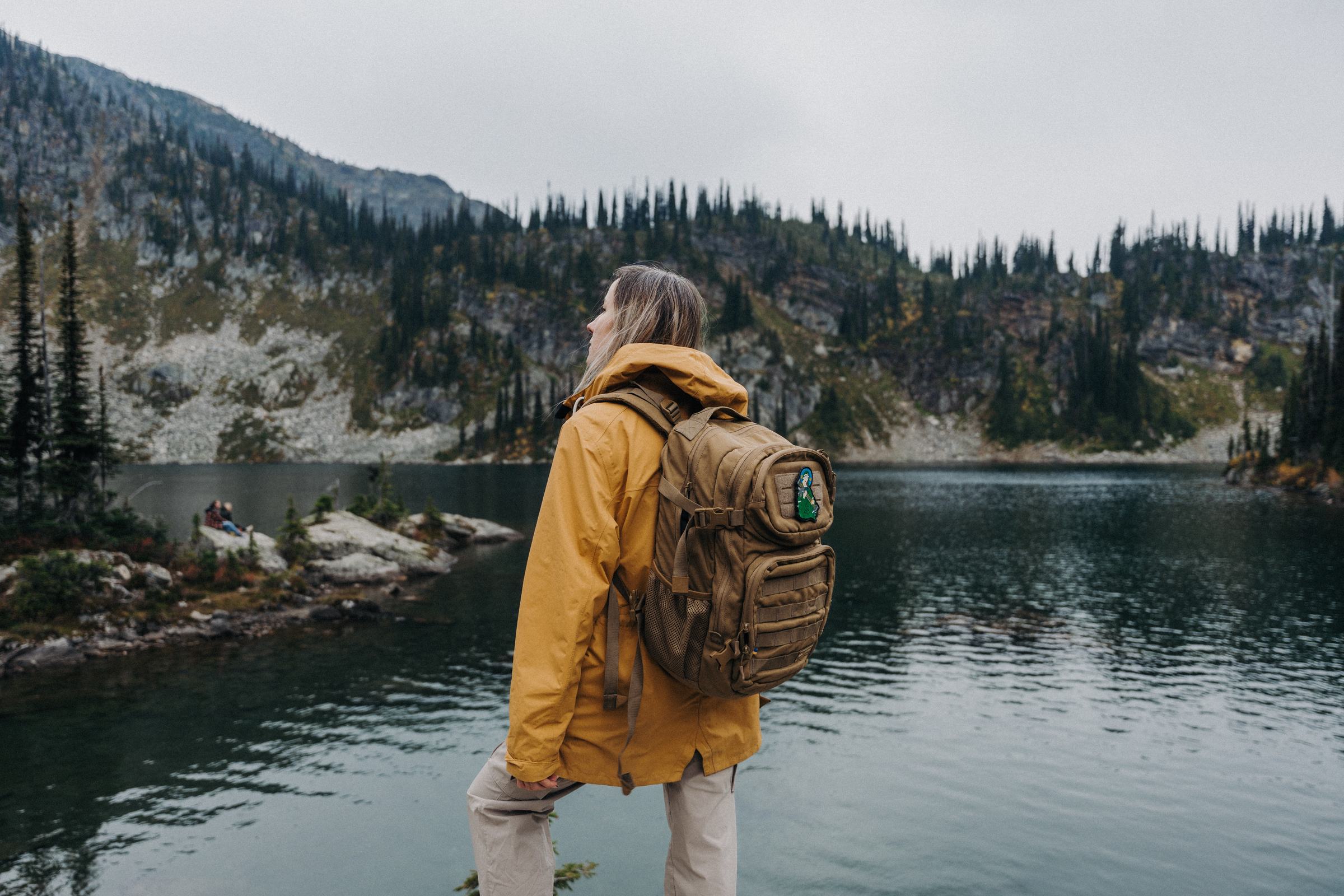 Hiker in a yellow jacket wearing a Saint Javelin backpack beside a mountain lake, Carpathian Mountains, Ukraine
