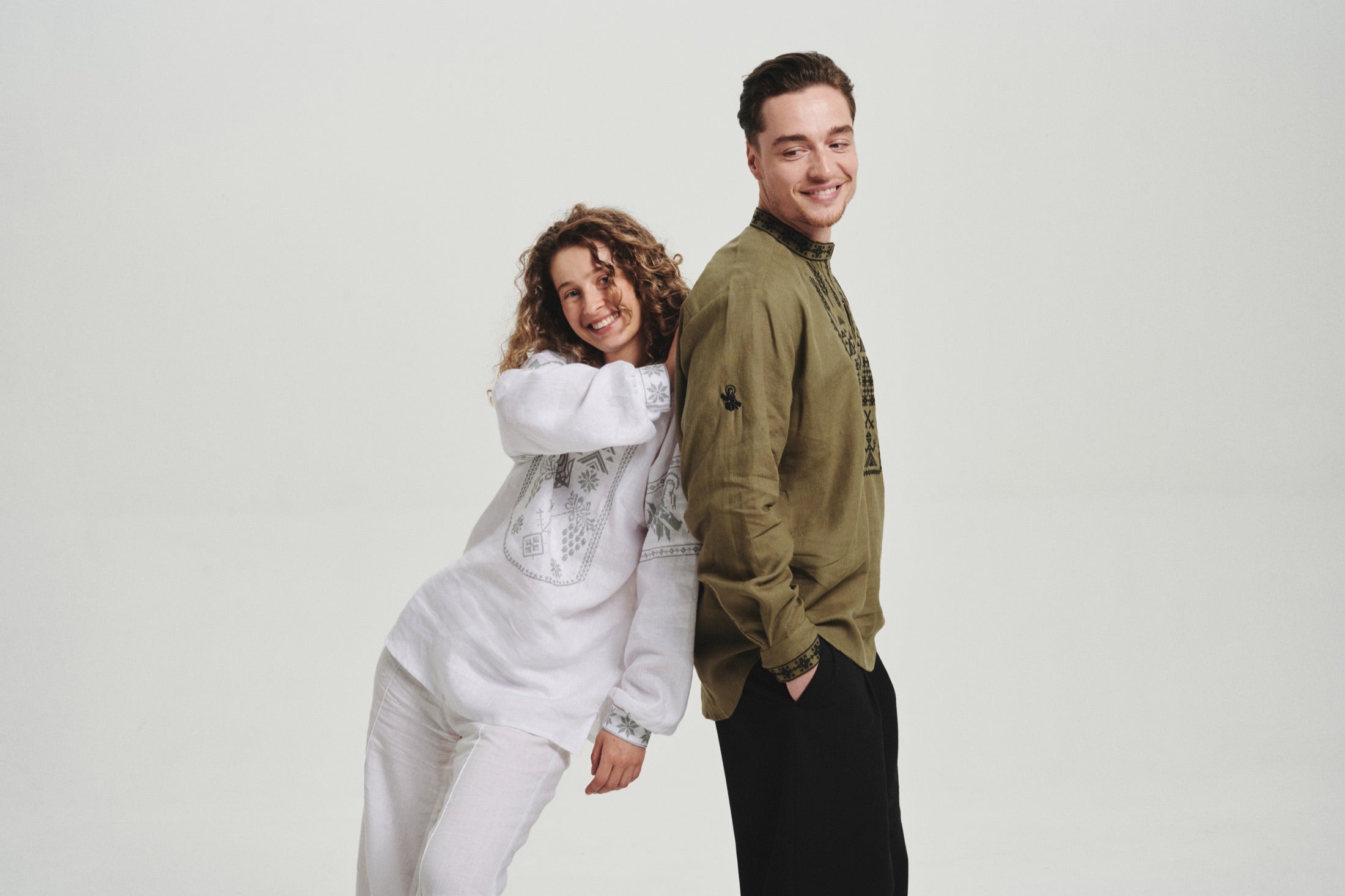 Two Ukrainian models standing back to back in embroidered linen vyshyvanka shirts, white and olive